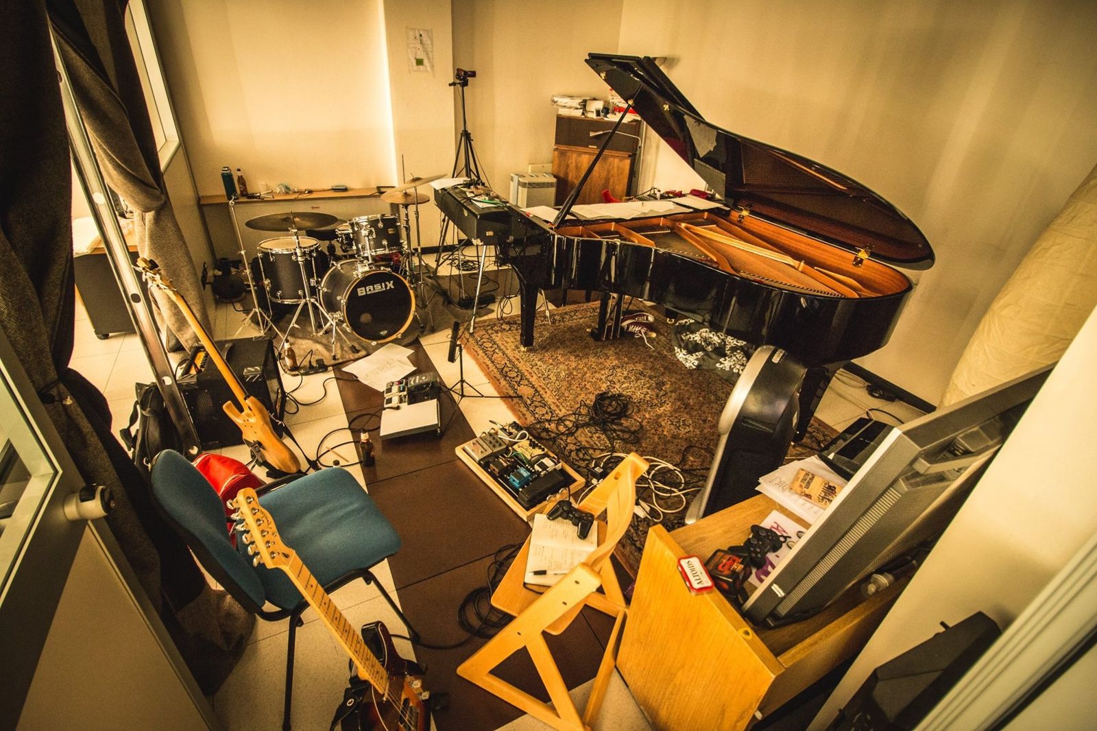 Una sala prove con pianoforte a coda aperto, batteria, chitarre e pedaliere sparse sul pavimento