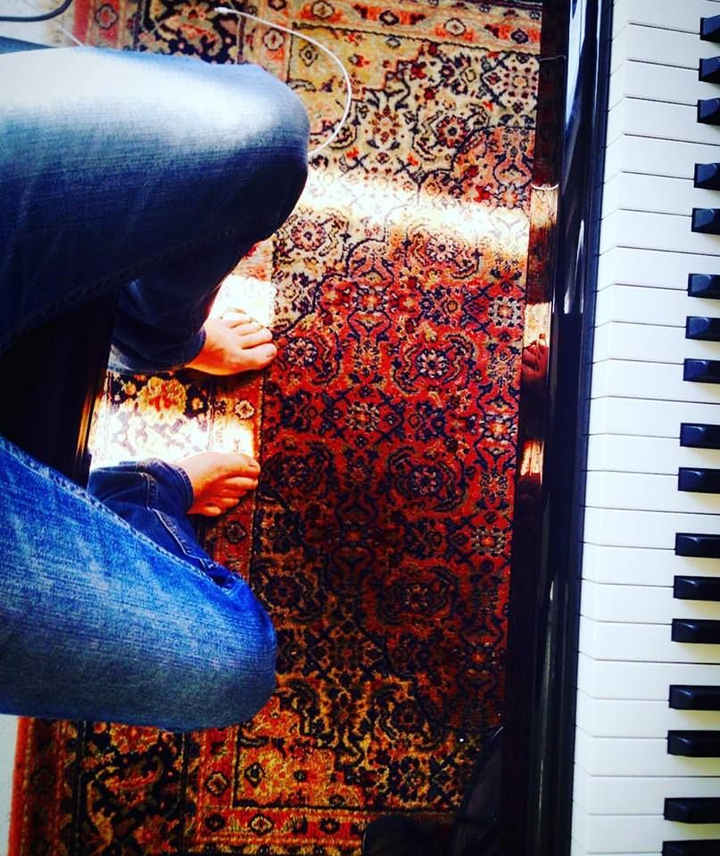 Piedi nudi su un tappeto persiano accanto alla tastiera di un pianoforte, visti dall'alto