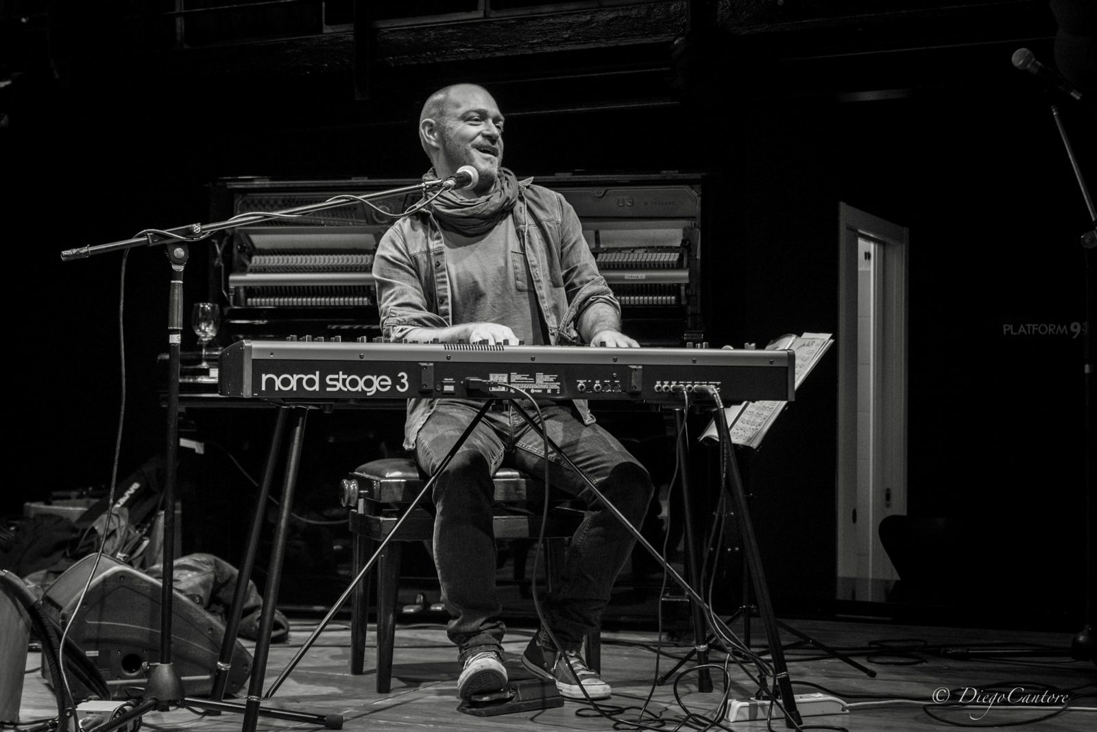 Paolo Censi sorridente sul palco, seduto a una tastiera Nord Stage 3, con un pianoforte verticale aperto alle spalle