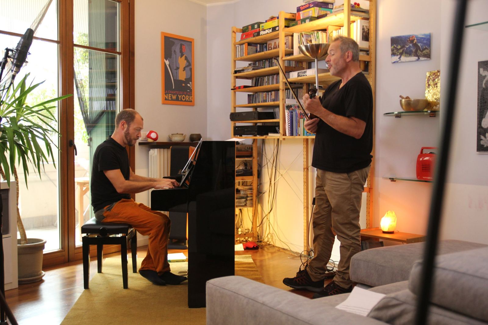 Paolo al pianoforte verticale e Milo Molteni al violino mentre suonano e cantano in un soggiorno pieno di dischi