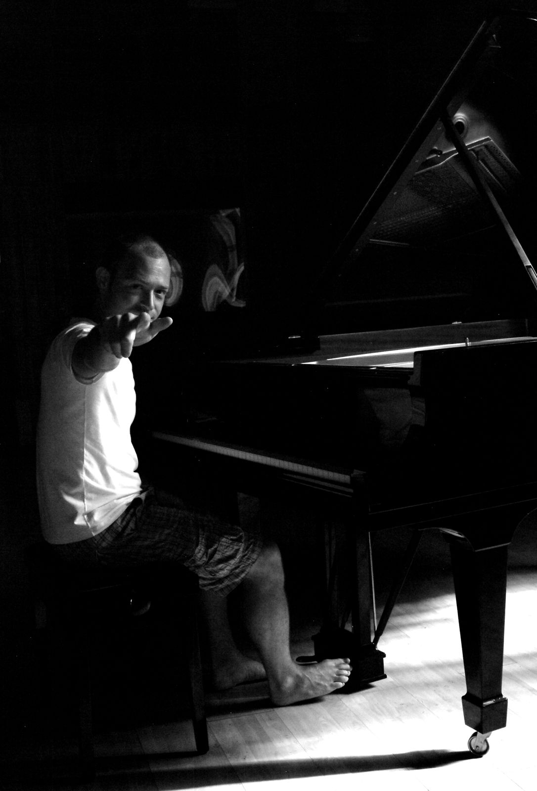 Ritratto in bianco e nero: Paolo Censi seduto al pianoforte a coda, a piedi nudi, tende la mano verso l'obiettivo