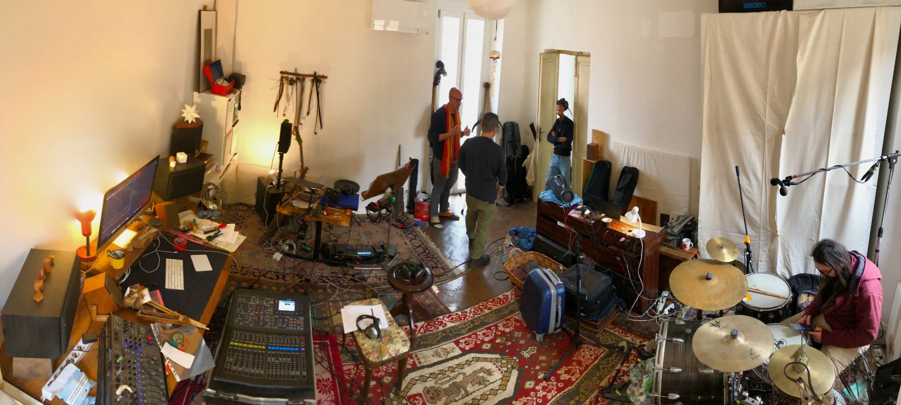 Panoramica della sala prove: tappeti, mixer, batteria e musicisti che parlano tra una registrazione e l'altra